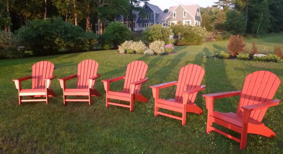Red plastic Adirondack chairs glisten in the rays of the setting sun after an early evening thundershower.