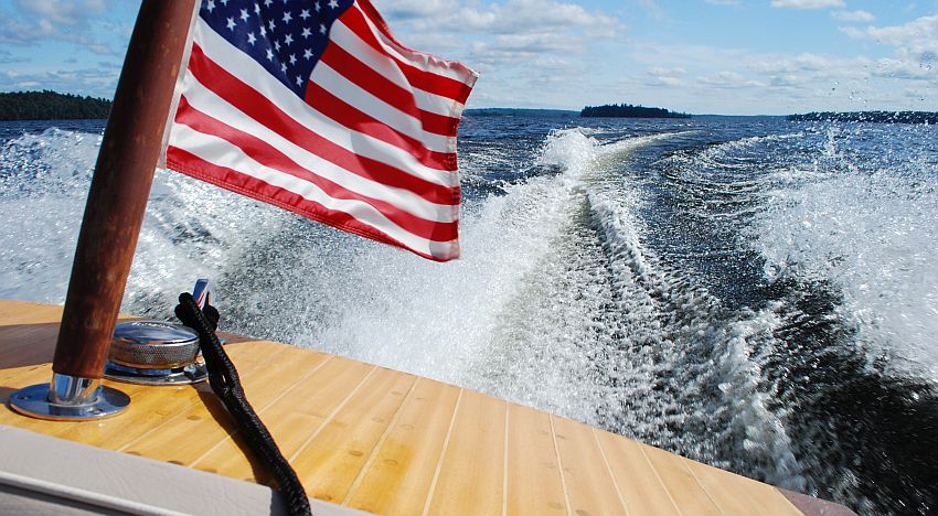 The Stars and Stripes snaps in the wind over the stern of a wooden motorboat racing down Great Pond. Photo by Frank L. Barkley, Jr.