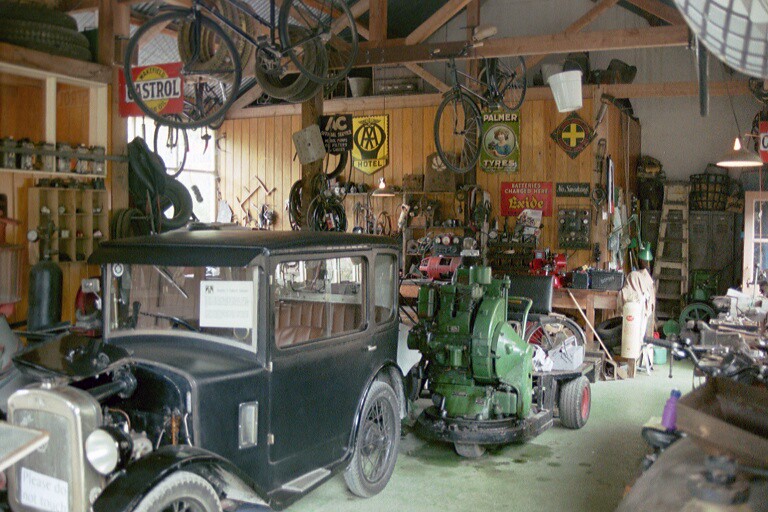 A vintage car, bicycles, tires, and miscellaneous parts and equipment inside a garage.