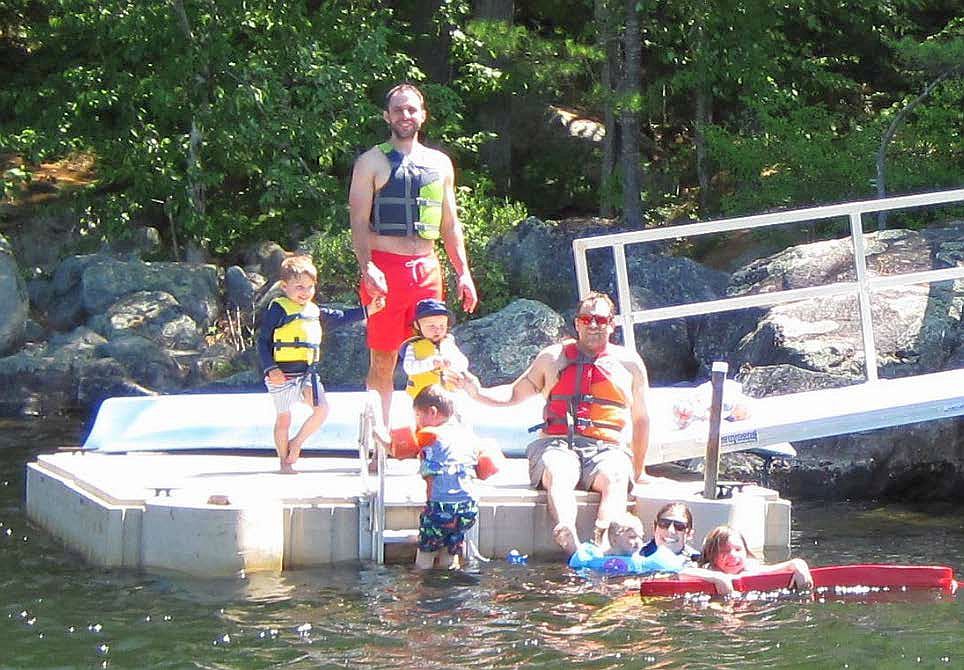 Standing on the dock from left to right are Wes, Mac, and Fiona Cook. Ben Whitt is coming up the ladder next to his dad Ryan (sitting on the dock) and his sister Maggie, mom Kate, and cousin Elli Cook (all still in the water).