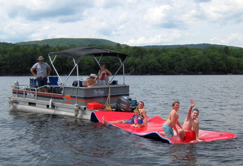 Pontoon boat with three adults pulling a floating mat with one adult and three children.