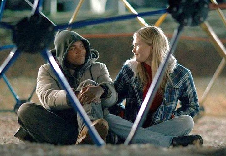 Two people sitting on the ground inside a jungle gym in a deserted playground at night.