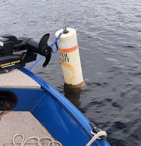 A buoy marking a water quality test site and the gunwale of a boat..